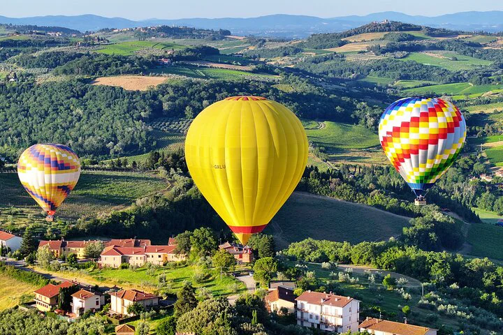 yellow hot air balloons above houses on tuscany hills