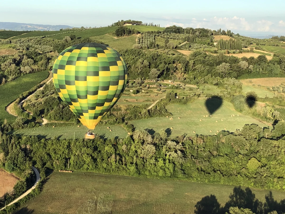 Green and yellow checkered hot air balloon floating over Tuscany