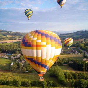 Hot air balloons floating over green countryside at sunrise, flight from Siena in Tuscany